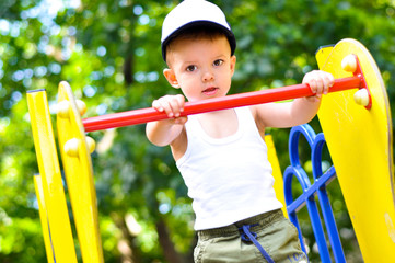 Fototapeta premium A cute two-year-old boy in a baseball cap sliding on a slide on a playground 