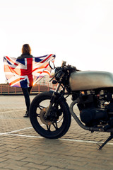 Obraz na płótnie Canvas Sexy biker woman on vintage custom caferacer motorcycle. Girl in black leather jacket with Britain flag. Urban roof parking, sunset in big city. Traveling and active hipster lifestyle. Girls power.