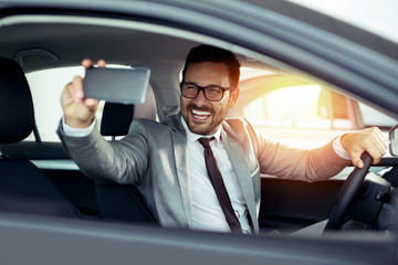 Businessman is choosing a new vehicle in car dealership and making photo on a smartphone