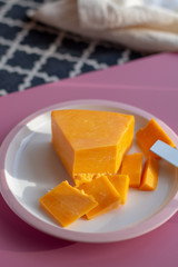 Triangle piece of British hard cow  dark yellow cheddar cheese on pink table