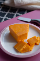 Triangle piece of British hard cow  dark yellow cheddar cheese on pink table