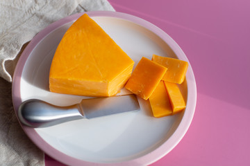 Triangle piece of British hard cow  dark yellow cheddar cheese on pink table