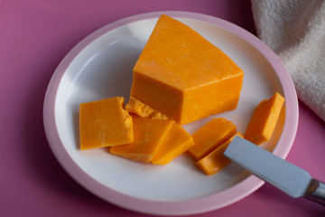 Triangle piece of British hard cow  dark yellow cheddar cheese on pink table