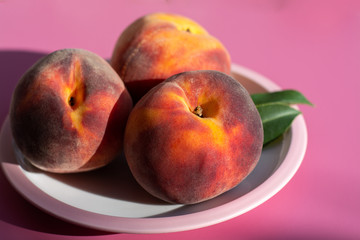 Three whole ripe peaches fruits close up on pink board and table