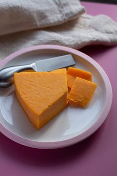 Triangle piece of British hard cow  dark yellow cheddar cheese on pink table