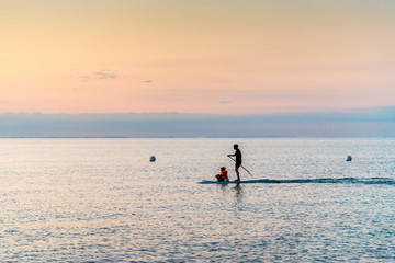 silhouette of father and son standing on Stand Up Paddle Board. SUP. in beatutiful sunset at the beach in a quiet scene.	