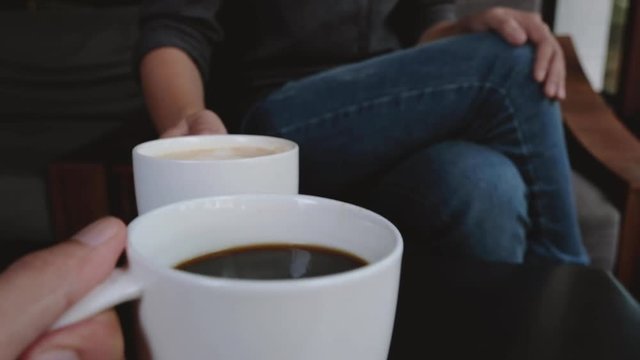 Close up image of two people clinking white coffee mugs in cafe