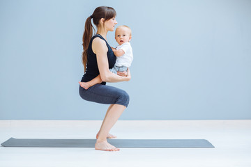 Obraz premium Sport, motherhood and active lifestyle concept - side view of young mother doing yoga with toddler baby at home. Squatting exercise.