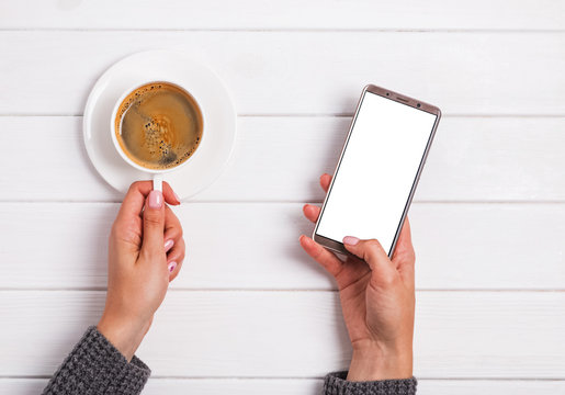 Woman's hands holding cup of coffee and using smarphone