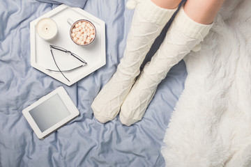 Woman's legs in socks and cup of cocoa with marshmallows.