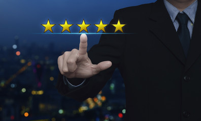 Businessman pressing five gold stars to increase rating over blur colorful night light city tower and skyscraper, Business and industry feedback concept