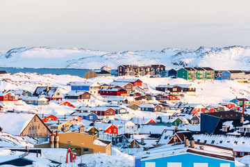 Lots of Inuit houses scattered on the hill in Nuuk city covered in snow with sea and mountains in the background, Greenland - obrazy, fototapety, plakaty