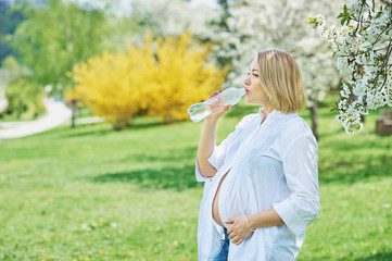 pregnant woman drinks water. Became ill in the heat. drinking balance during pregnancy. drinking water bottle of water in her hand in pregnant diet