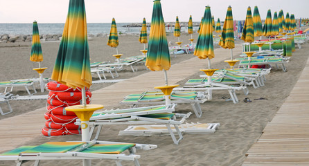 closed umbrellas and deck chairs on the beach at the end of the