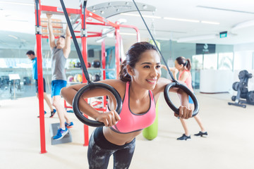 Cheerful fit young woman exercising with gymnastic rings during routine workout in a trendy fitness center with modern equipment for functional training