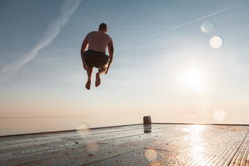 The guy is jumping from the pier. The sky and the sun. Summer. The man in flight.
