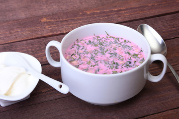 Popular spring cold soup okroshka with yoghurt. Okroshka in a bowl, sour cream and slices bread on wooden table. Selective focus