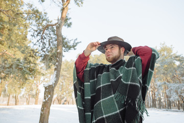 Male hiker in vivid poncho. Tourist in round hat exploring freedom and nature. Winter snowy forest landscape Adventure active vacations and cold weather.
