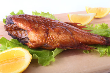 Smoked fish and lemon on green lettuce leaves on Wooden cutting board isolated on white background.