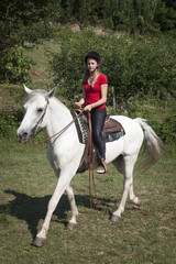 Fototapeta premium young teen girl in red shirt on white horse in green surroundings