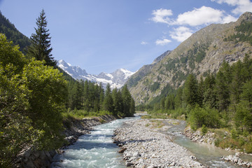 Fototapeta na wymiar mountain stream in italian national park gran paradiso with snow capped mountains in the background