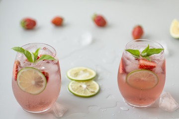 Glass of strawberry lemonade with pieces of strawberry, lime and fresh mint. Fresh summer bright cocktail.