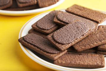 Chocolate cookies or biscuits and cream in, on yellow background. Close up sweet unhealthy snack or kids or adults.