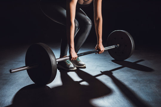 cropped image of female athlete working out with barbell, black background