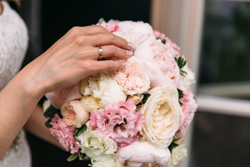 Obraz na płótnie Canvas Close-up of a cropped frame, the hand of a young girl with an engagement ring on a ring finger. Gently touches the wedding bouquet of peonies. Wedding day, bouquet of the bride. wedding ring
