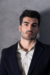 Portrait of a serious handsome businessman in a black suit in front of a grey wall in a studio.