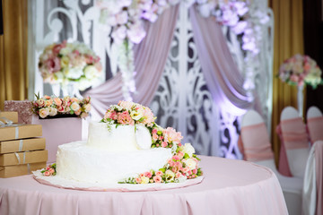 A large white wedding cake on the table, decorated with fresh flowers. Preparation for the wedding, decorating and idea for the wedding ceremony.