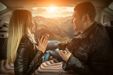 Couple in car. Blonde female and male drink tea in trunk in them