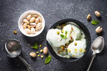 Pistachios ice cream in bowl on black stone table.