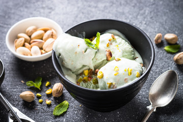 Pistachios ice cream in bowl on black stone table.