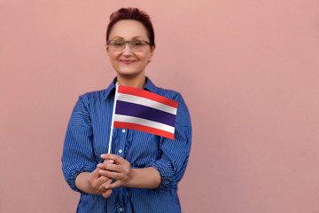 Thailand flag. Woman holding Thai flag. Nice portrait of middle aged lady 40 50 years old with a national flag over pink wall background.