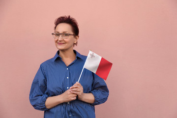 Malta flag. Woman holding Maltese flag. Nice portrait of middle aged lady 40 50 years old with a national flag over pink wall background. Learning English / Visit Malta concept.