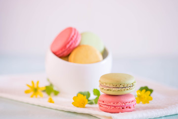 Macarons in white porcelain bowl with nice yellow flowers on blue wooden table