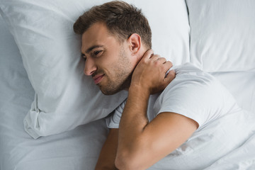 top view of young man lying in bed and suffering from pain in neck