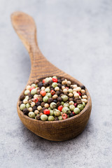 Peppercorn mix in a wooden bowl on grey table.