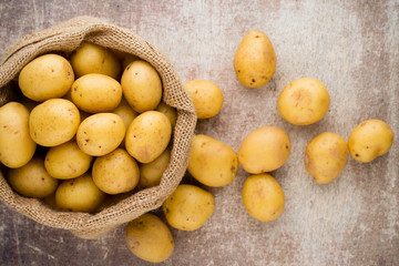 Sack of fresh raw potatoes on wooden background, top view.
