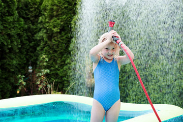 blondes mädchen spielt im pool mit gartenschlauch