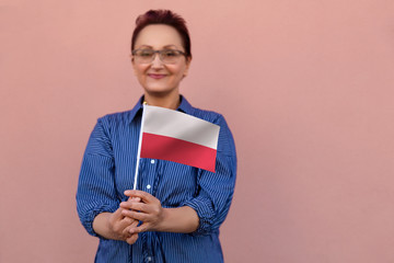 Poland flag. Woman holding Polish flag. Nice portrait of middle aged lady 40 50 years old with a national flag over pink wall background outdoors. - 216956429