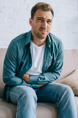 Fototapeta premium young man with stomach ache sitting on sofa and looking at camera