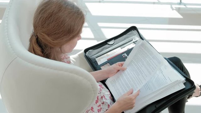 attractive businesswoman sitting on a white chair in a glass office and checks documents