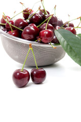 Steel colander with red sweet cherry isolated on a white background..
