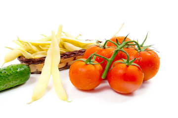 Fresh young pods of beans with beans, bunch of the fresh red tomatoes and several green cucumber with water drops on white background..