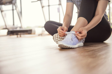 Woman tying running shoes on black floor background in gym fitness with sunlight. copy space.