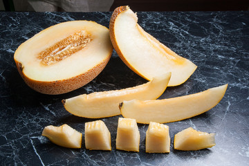Half and sliced honeydew melon fruit on dark marble background..