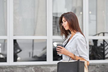 Young slim girl with long brunette hair going out from shop carrying bags.