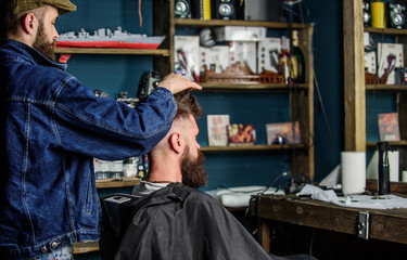 Man with beard and mustache in hairdressers chair, shelves on background. Barber styling hair of bearded client with wax by hands. Barbershop concept. Hipster client with fresh haircut or hairstyle